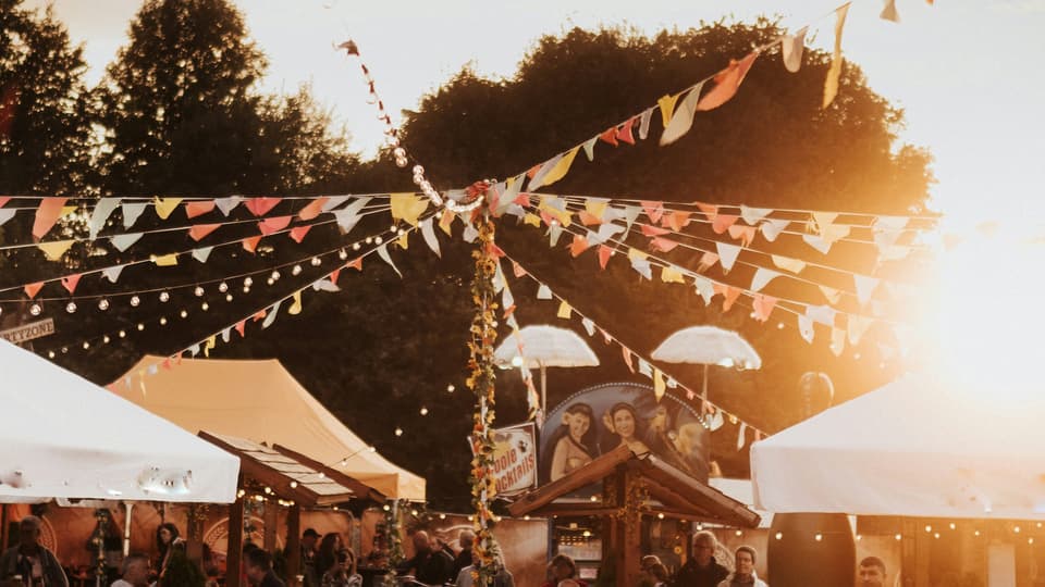 Festival med besökare, tält och vimplar i kvällsljus.