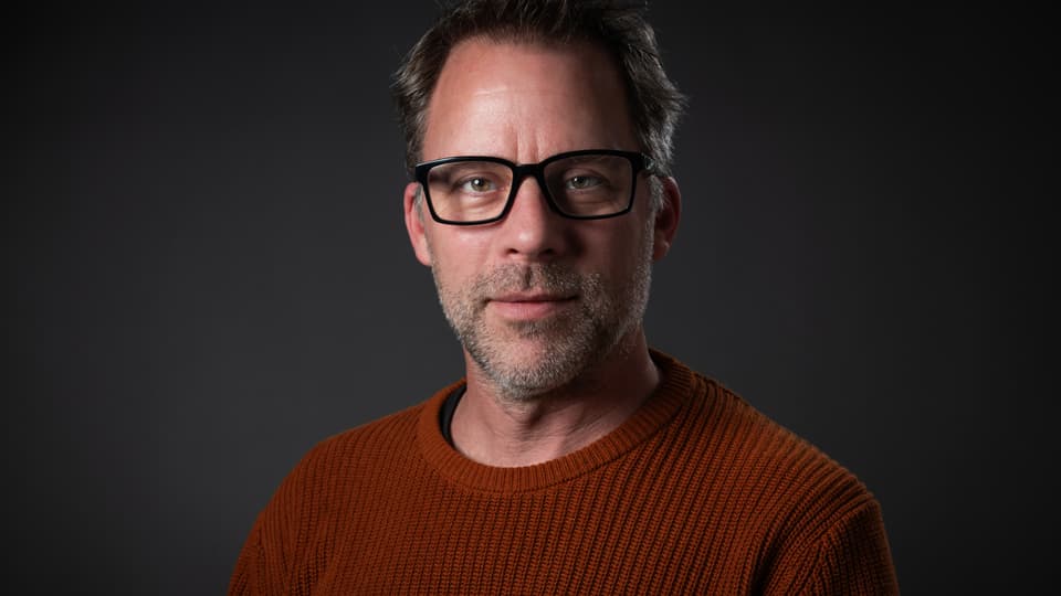 Man in dark glasses and dark red knitted sweater poses in front of the camera.